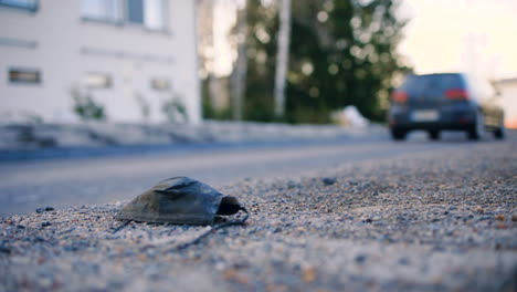 Slomo-shot-of-car-driving-past-black-protective-face-mask-on-ground