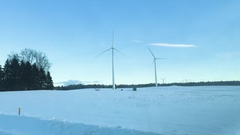 driving past wind turbines in a snow-covered field during winter in new york state, usa. renewable energy structures stand tall against a clear blue sky, blending technology with a natural landscape.