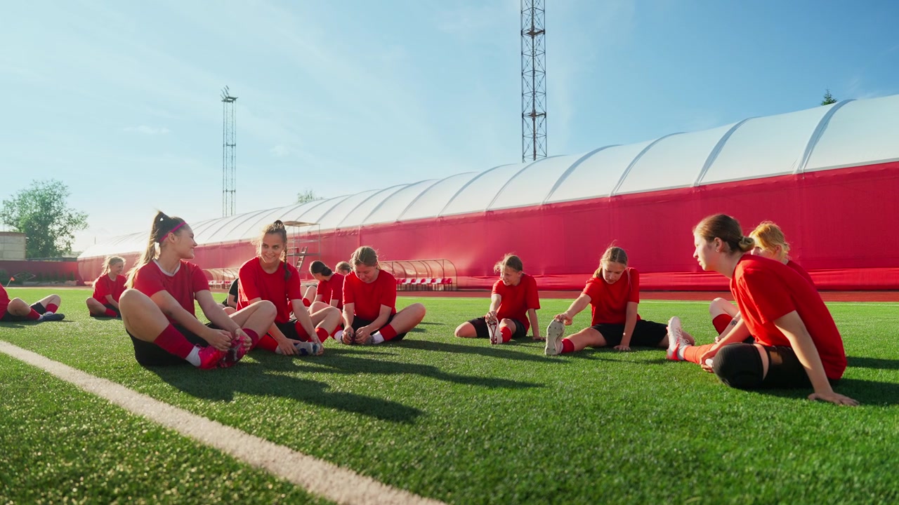 Ungt kvinnligt fotbollslag som sträcker ut sig tillsammans på planen.