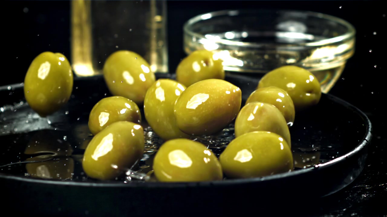 Olive verdi fresche che schizzano nell'olio d'oliva al rallentatore