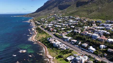 aerial orbit of vacation homes on the coast of a scenic ocean vista with steep mountains, rocky shore and sea green waters near cape town south africa