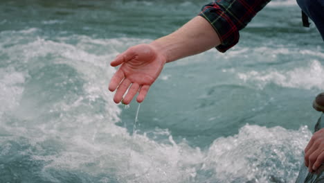 junge sitzt am felsufer. wanderer berührt wasser mit der hand im flussfluss