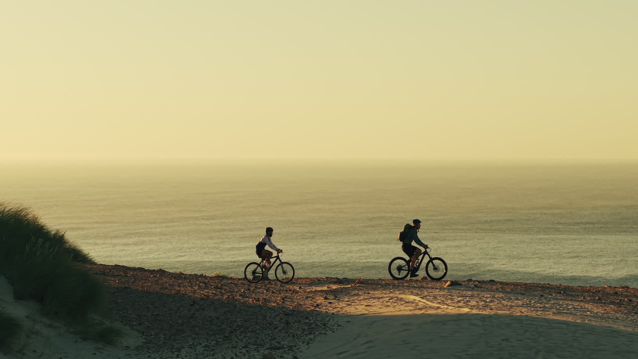 Due ciclisti in mountain bike lungo le dune di sabbia costiere al tramonto