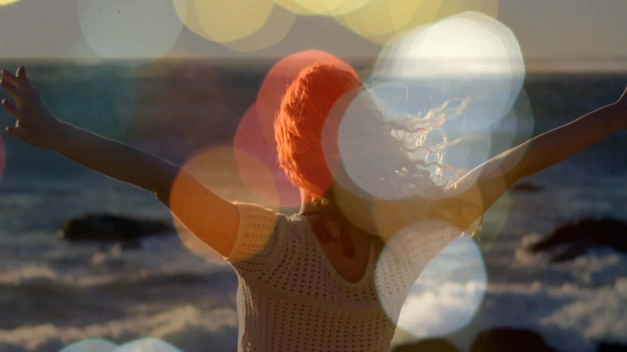 Vrouw met opgeheven armen op rotsachtige kust, met verschuivende bokeh-effecten en de wind die haar haar laat wapperen, marketing