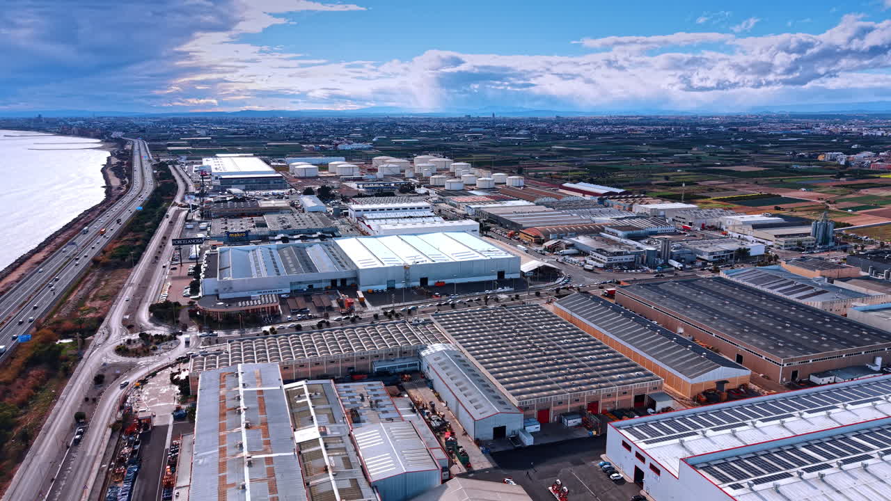 Madrid, Spain, 8 August 2025: Panoramic aerial view of industrial district and coastal highway. Wide perspective of logistics park, sea shore, multi-lane road, storage tanks, warehouses, cloud sky