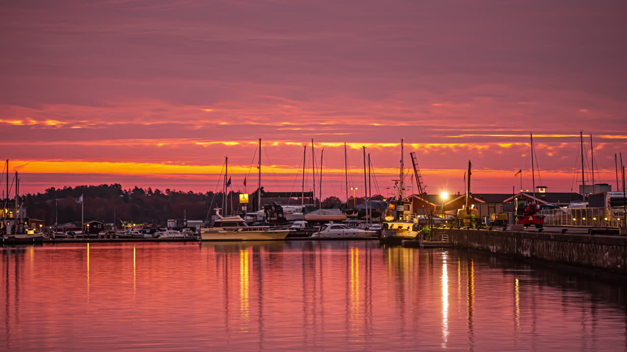 Night to sunrise timelapse of work going on under halogen light at a port with boats and yachts at sunrise. Beautiful landscape of the harbor by the coast