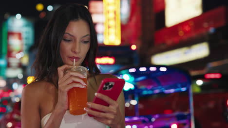 woman enjoying a drink and using her phone in a vibrant city at night
