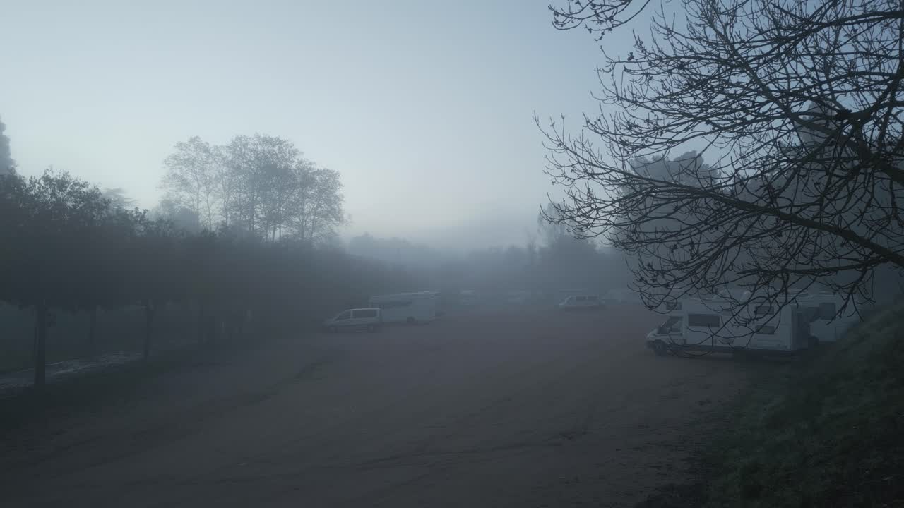 Dense fog slowly enveloping camping car park in catalonia, spain, creating ethereal atmosphere during soft morning light with low visibility and serene landscape