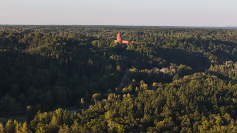 turaida castle tower peaking above the verdant landscapes of sigulda, latvia; slow aerial approach towards the newly reconstructed medieval castle.