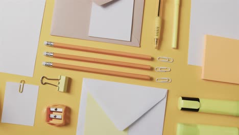 overhead view of pens, pencils and stationery arranged on yellow background, in slow motion