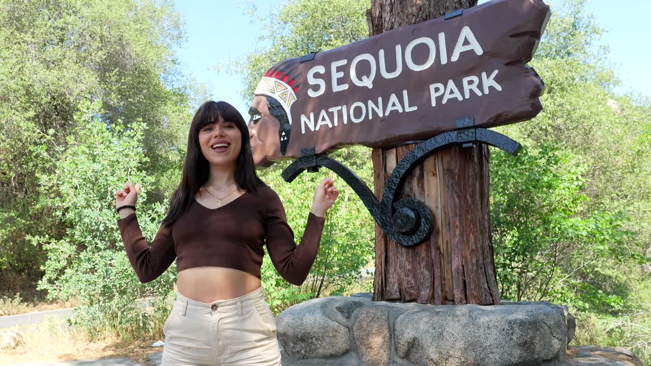 Giovane donna felice in posa al cartello d'ingresso del Parco Nazionale di Sequoia