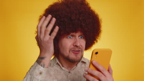 man with afro wig looking at his phone with a surprised expression