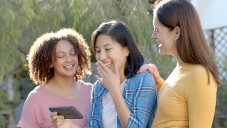watching video on smartphone, three women friends laughing and enjoying time together