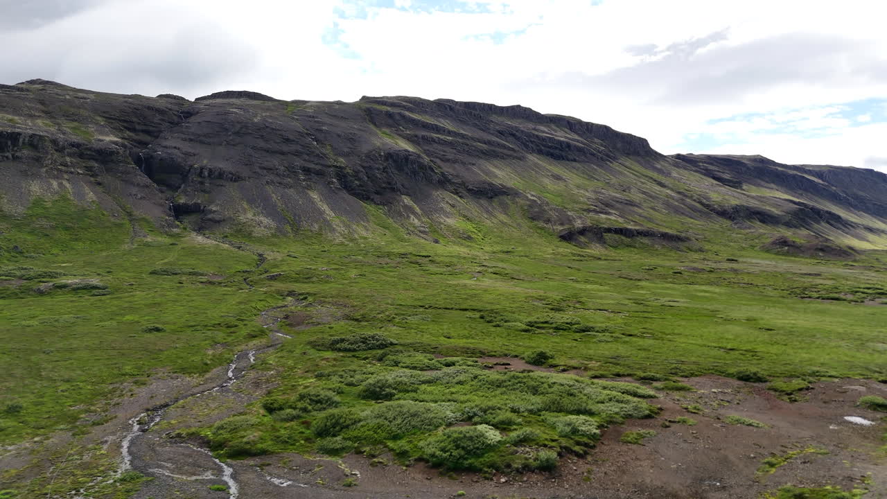 Luftdronevisning av en grusvei som følger fjellene langs Hvammsfjörður-fjorden i Vesturland, Island, og viser frem avsidesliggende høyland, grønne daler og dramatiske vulkanske skråninger