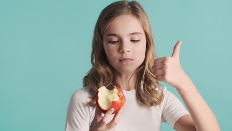 teenage caucasian girl in pijamas eating an apple and smiling.