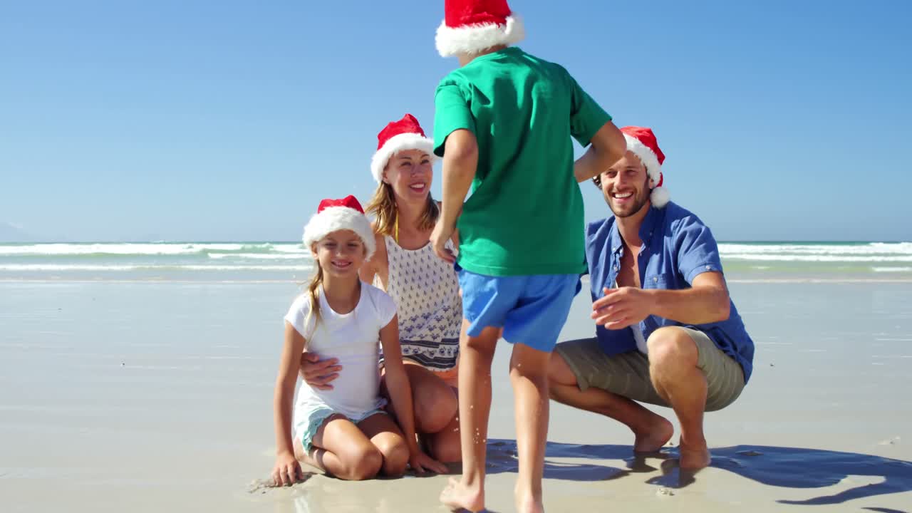 Familia feliz con gorros de Papá Noel posando en la playa