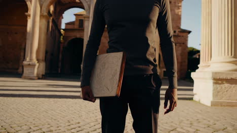 man holding a book in front of ancient roman architecture