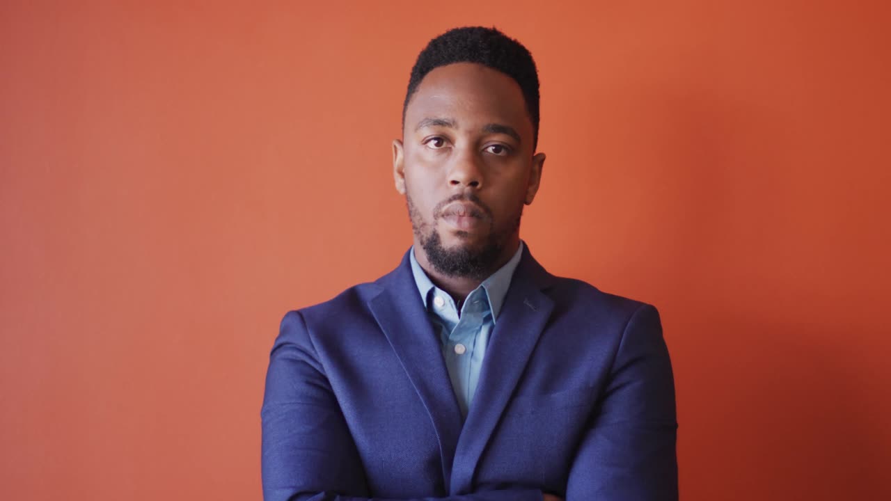 Video of serious african american man looking at camera on orange background