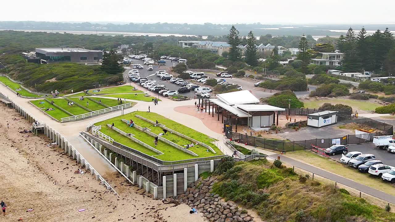 Drone footage captures a vibrant coastal park with green spaces, pathways, and beach access in Ocean Grove, Victoria