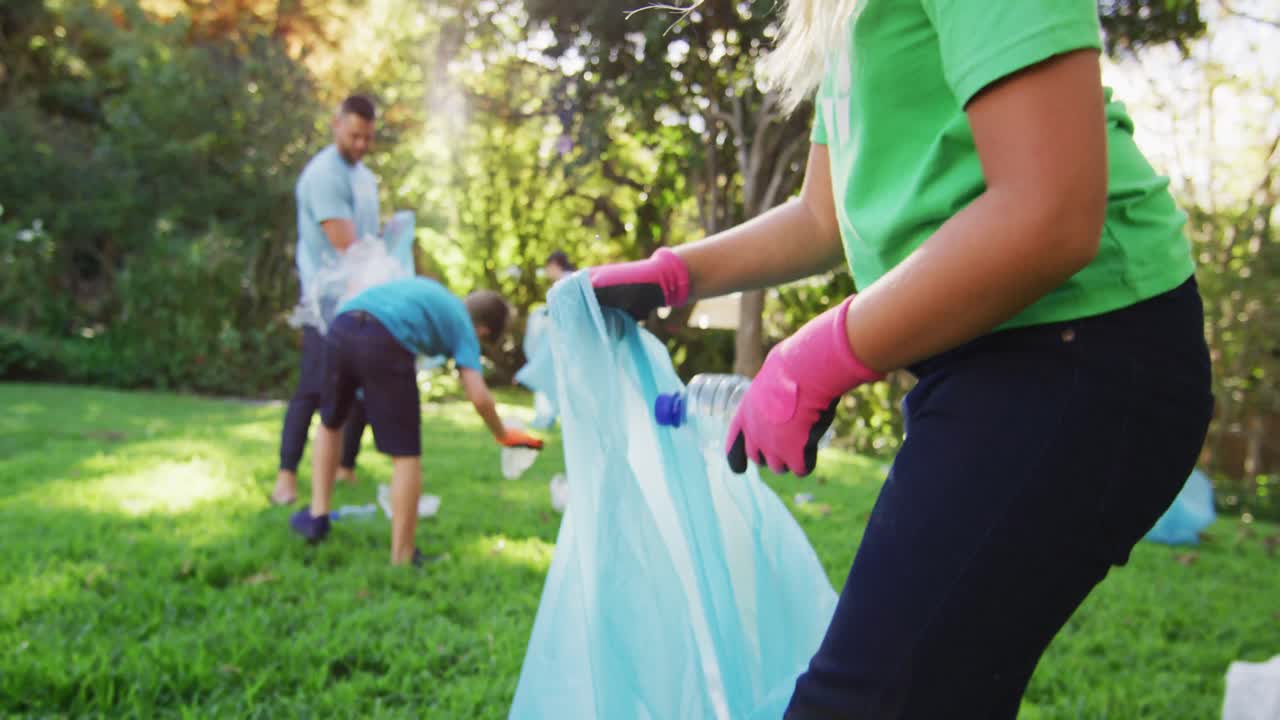 Figlia caucasica sorridente che tiene un sacco dei rifiuti, raccogliendo plastica con i genitori e il fratello