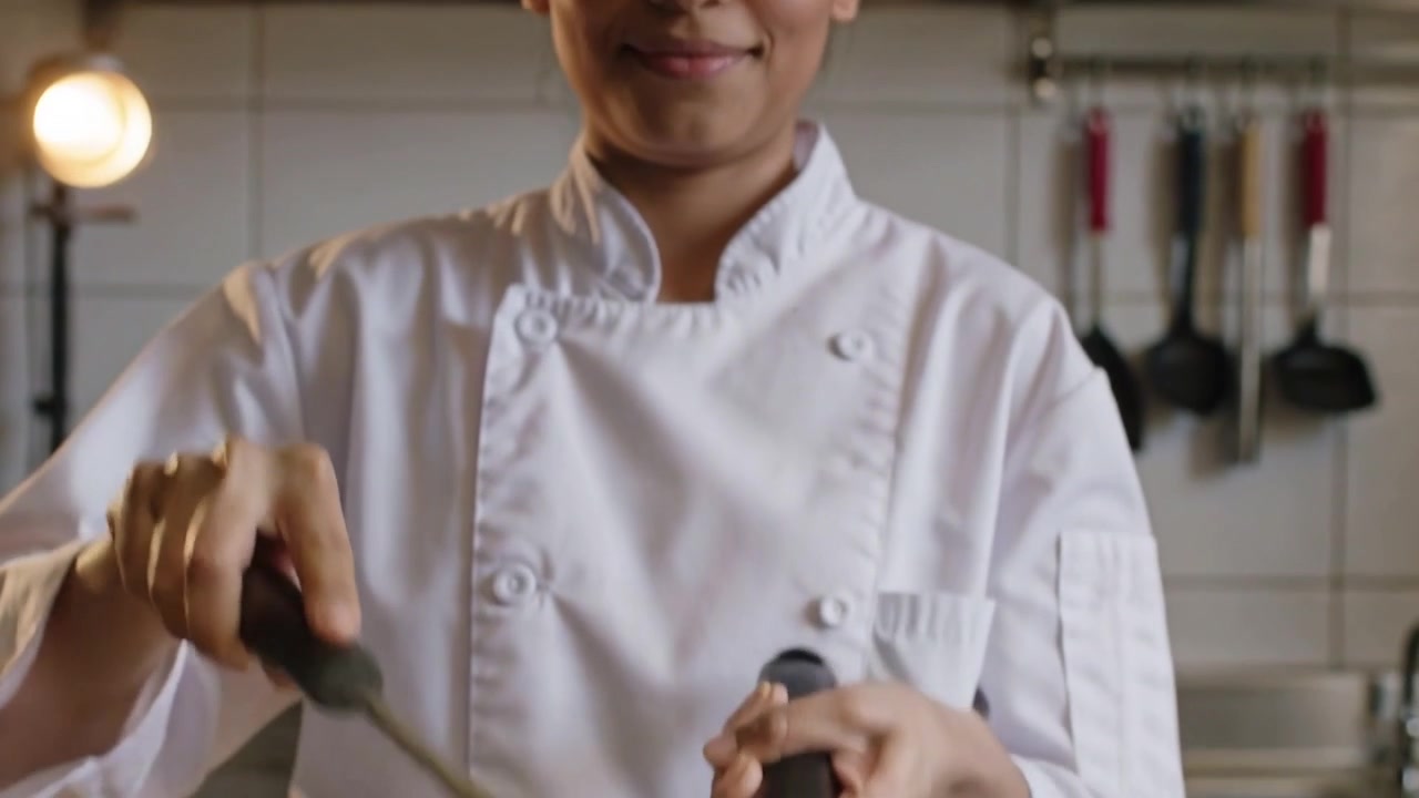 Inclinando la padella, uno chef in giacca bianca raschia e fa saltare il cibo sul fornello con una spatola per cucinarlo.