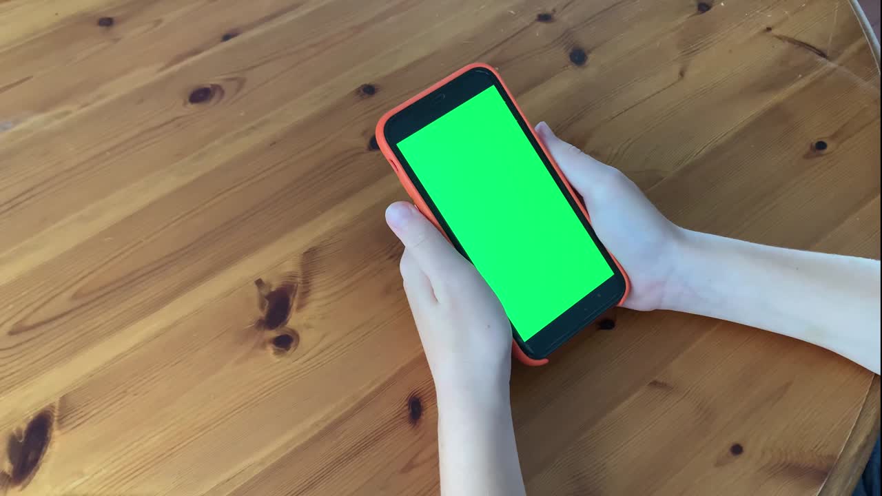 Young teenager boy hands using green screen smartphone sitting on the table. Online business communication. Chromakey mock-up. Tapping empty touchscreen. Social network. Internet chatting.