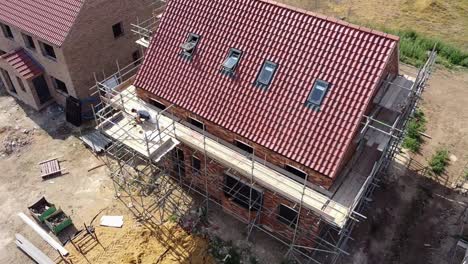 rotating aerial view of a scaffolded new build house under construction, showing the front elevation and the gable end