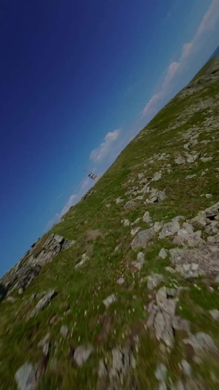 FPV drone flies over green slopes and rugged cliffs at Pointe du Raz with open ocean views