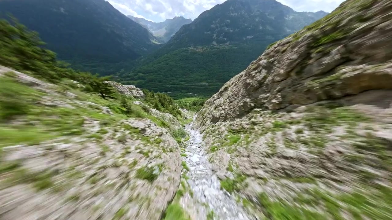Drone da corsa FPV si tuffa ad alta velocità lungo un ripido canalone montano italiano fiancheggiato da alberi e pietre sciolte verso la valle sottostante