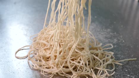 close-up footage of chef scattering egg noodles on shiny silver table