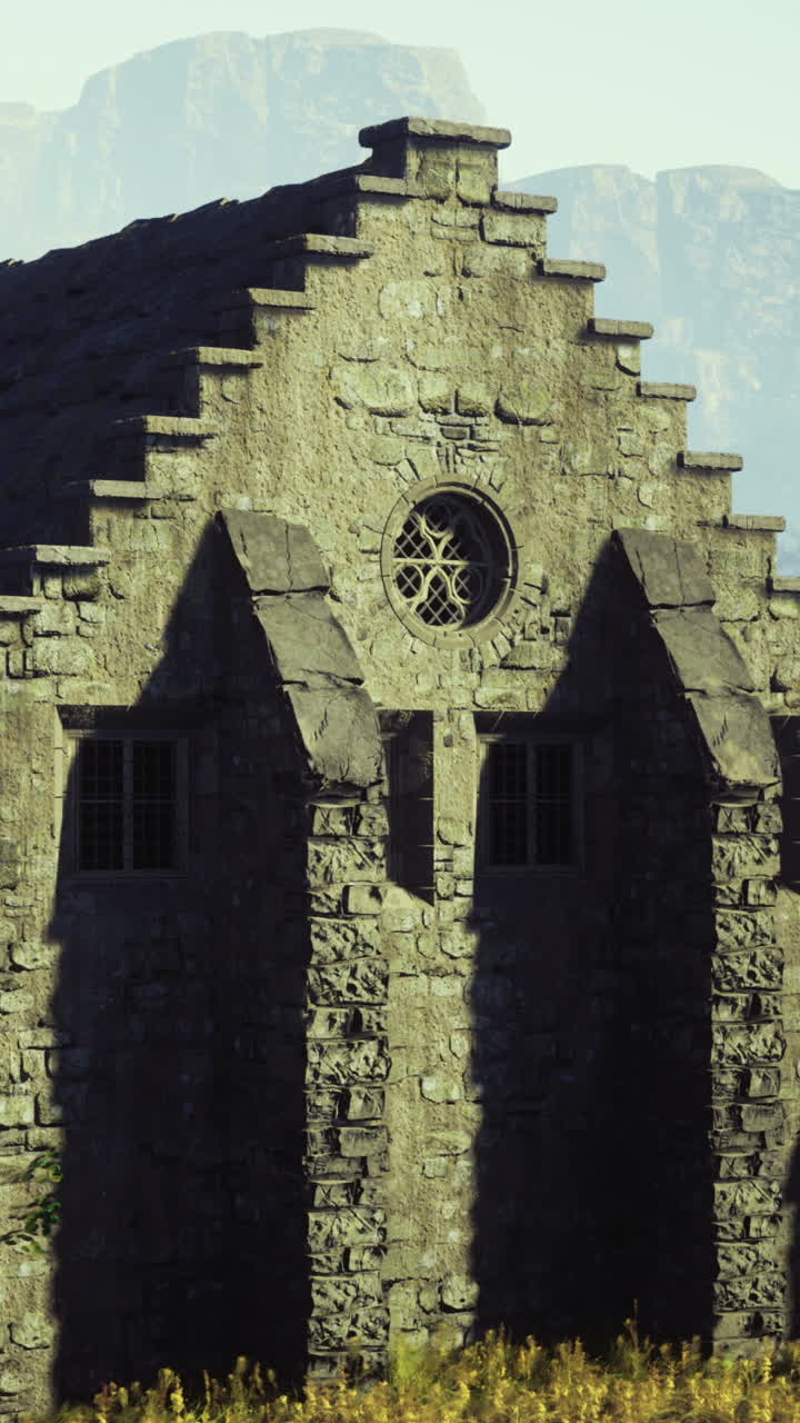 Edifício histórico de pedra ergue-se imponente em paisagem montanhosa sob a luz do sol.