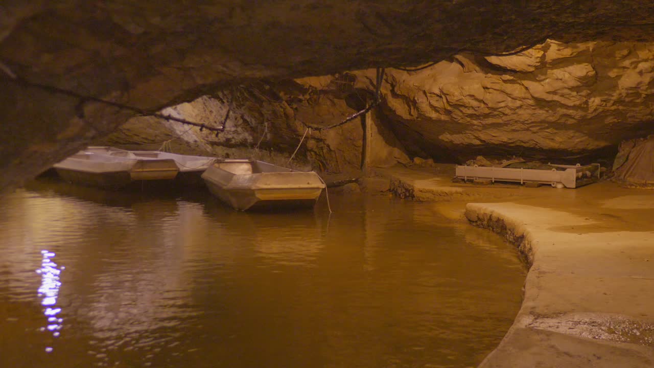 The dark, impressive interior of a subterranean river cave in Ariège, France. Features a pool of water and small boats, highlighting one of Europe's largest underground rivers