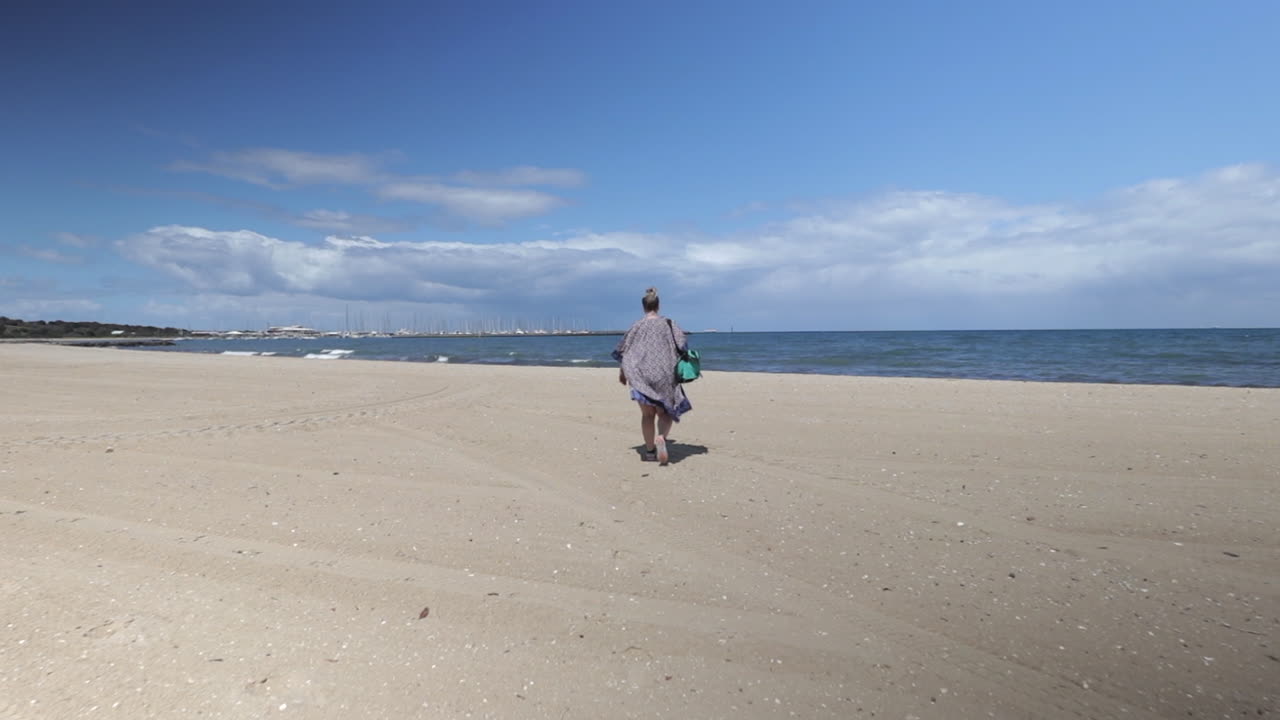 mujer con kimono caminando hacia el mar en la playa de hampton bay, melbourne, australia, día soleado, toma amplia