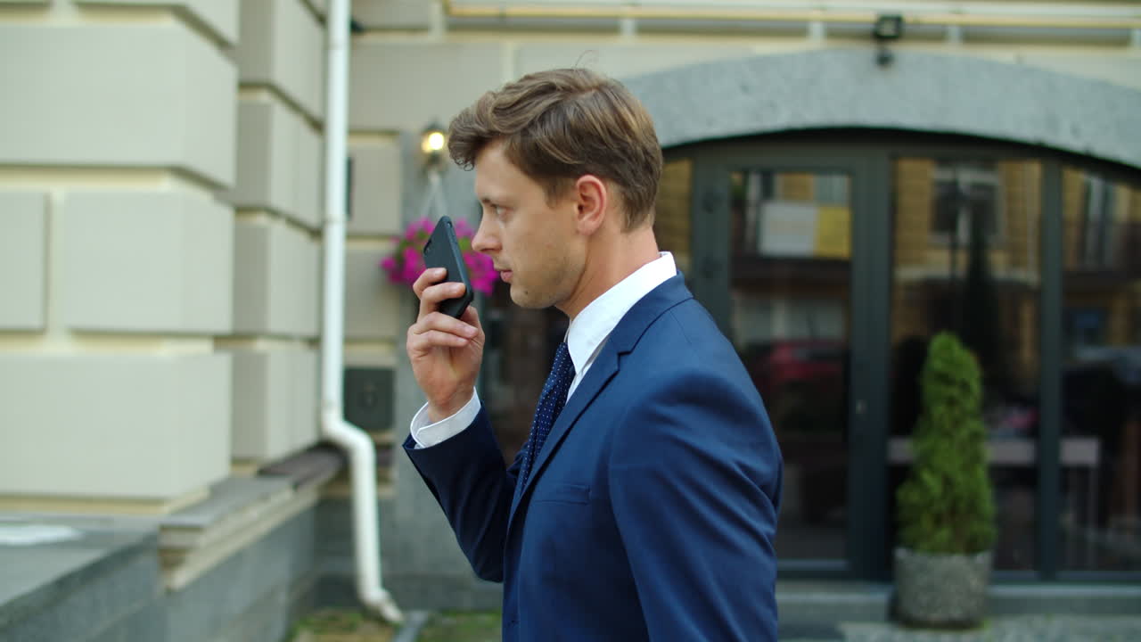 자신감 있는 사업가 가 야외 에서 휴대 전화 로 음성 메시지 를 녹음 하고 있다