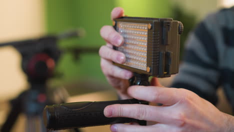 lighting operator adjusting led light on camera rig while preparing for shoot in studio. focused on setting up professional gear in production environment