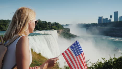 frau mit usa-flagge bewundert blick auf die niagarafälle von der amerikanischen küste