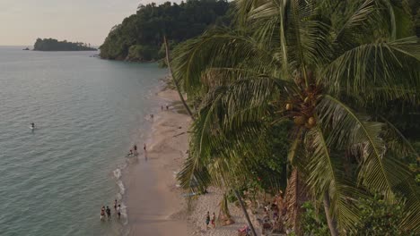 tropical island drone, bird’s eye view tilt up shot with tropical palm trees, islands with white sand beach and small beach bars and restaurants and bungalows with domestic tourists