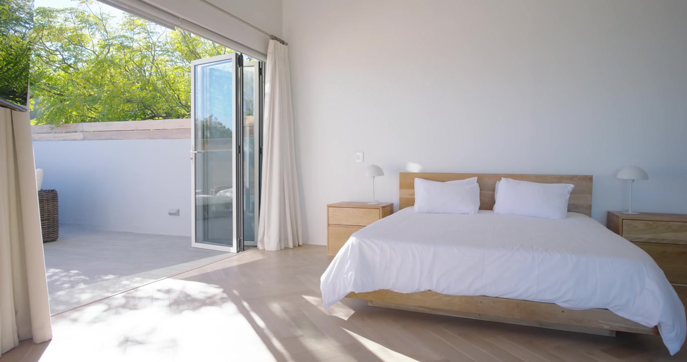 La telecamera si allontana e scorre a destra per rivelare un letto king-size e una terrazza all'interno della camera da letto.