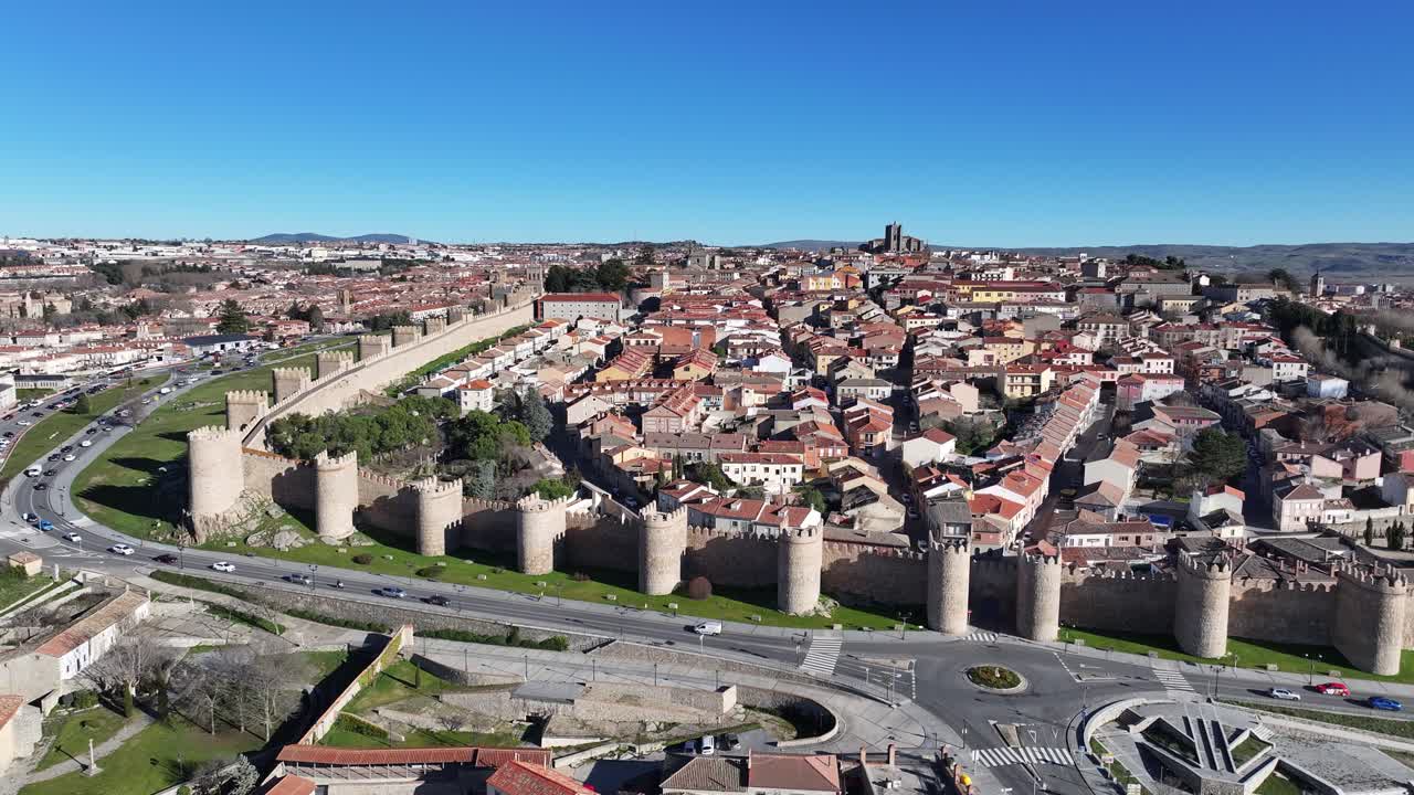 voo lateral na cidade do patrimônio mundial de avila vendo sua muralha medieval com suas casas internas e suas áreas verdes com uma estrada veículos circulando em um dia de inverno com um céu azul españa