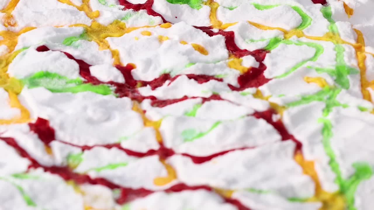 Vibrant red, green, and yellow liquids create intricate patterns on a textured white surface.