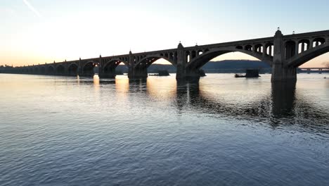 aerial flight over susquehanna river during golden sunset with silhouette of bridge with arches in the evening