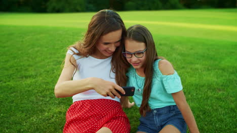 Frau-Und-Mädchen-Sitzen-Auf-Gras.-Mutter-Und-Tochter-Schauen-Sich-Ein-Video-Auf-Dem-Smartphone-An