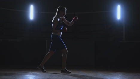 training a beautiful female boxer doing punches in a dark room. steadicam shot. preparation for self-defense and fight in the ring