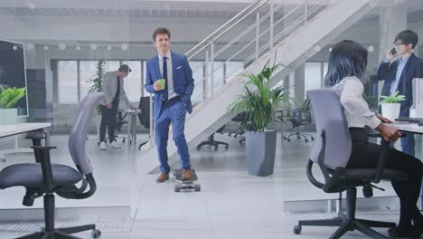young happy handsome manager wearing a suit and tie rides a longboard. he's holding a cup of coffee. diverse and motivated business people work on computers in modern open office.