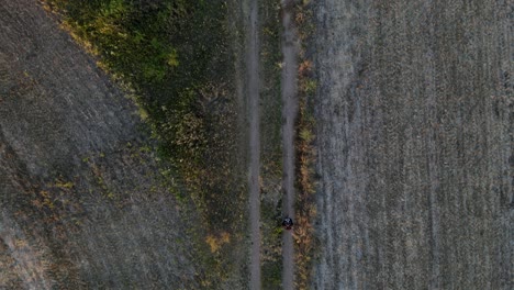 Person-hiking-along-a-straight-path-in-between-dry-fields-and-meadows