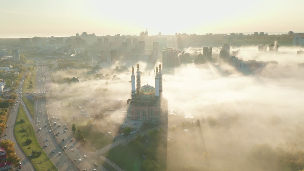 Veduta aerea dall'alto di una moschea con minareti dorati alla luce del sole e nella nebbia con foresta, strada ed edifici cittadini. Moschea Ar-Raheem nella città di Ufa