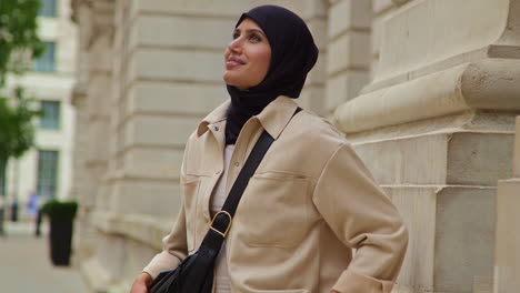 portrait of smiling muslim businesswoman wearing hijab and modern business suit standing outside city office buildings 2