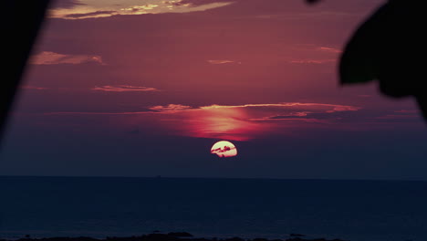 glowing sun setting beyond dark clouds over dusking ocean horizon