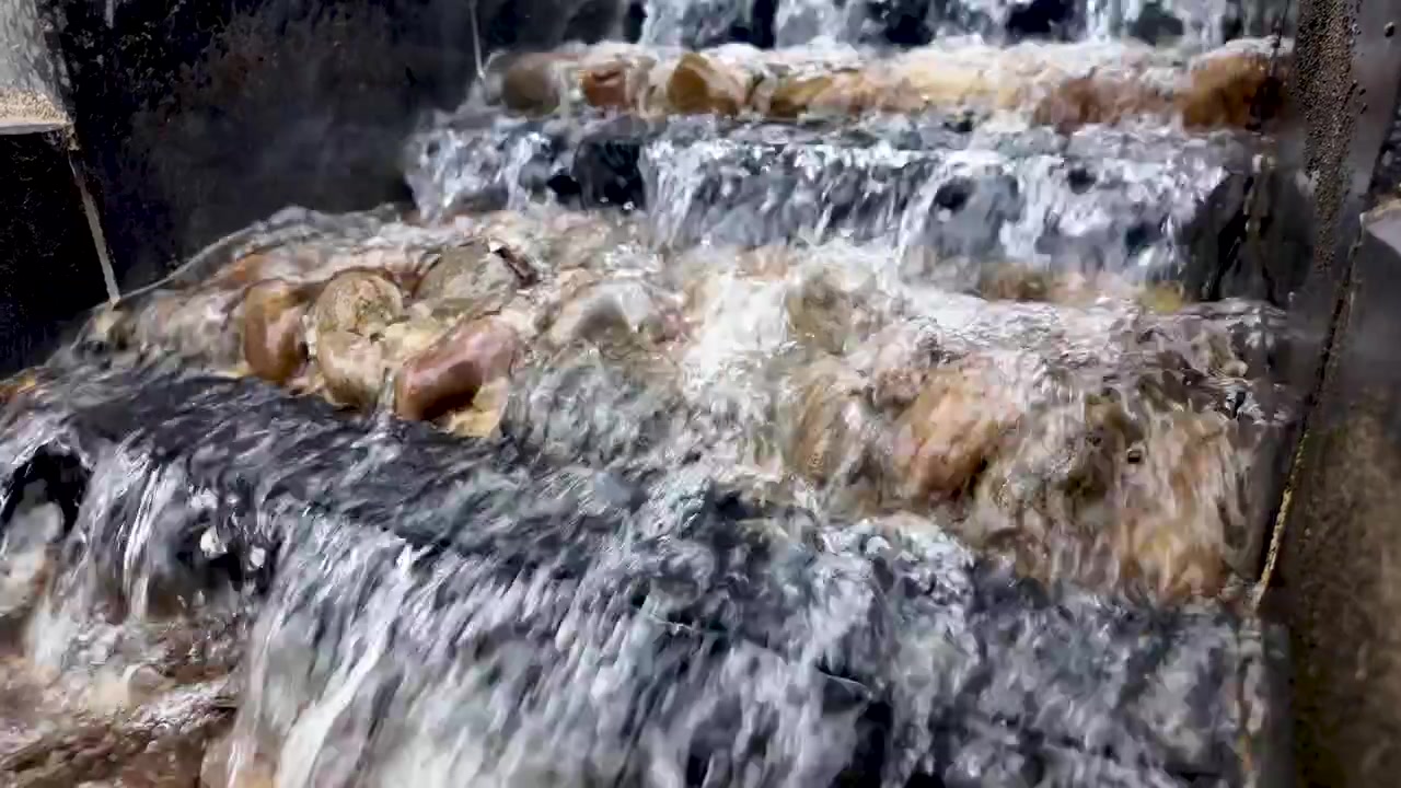 Primo piano dell'acqua che scende a cascata da una fontana rocciosa a più livelli in un giardino. Rallentatore