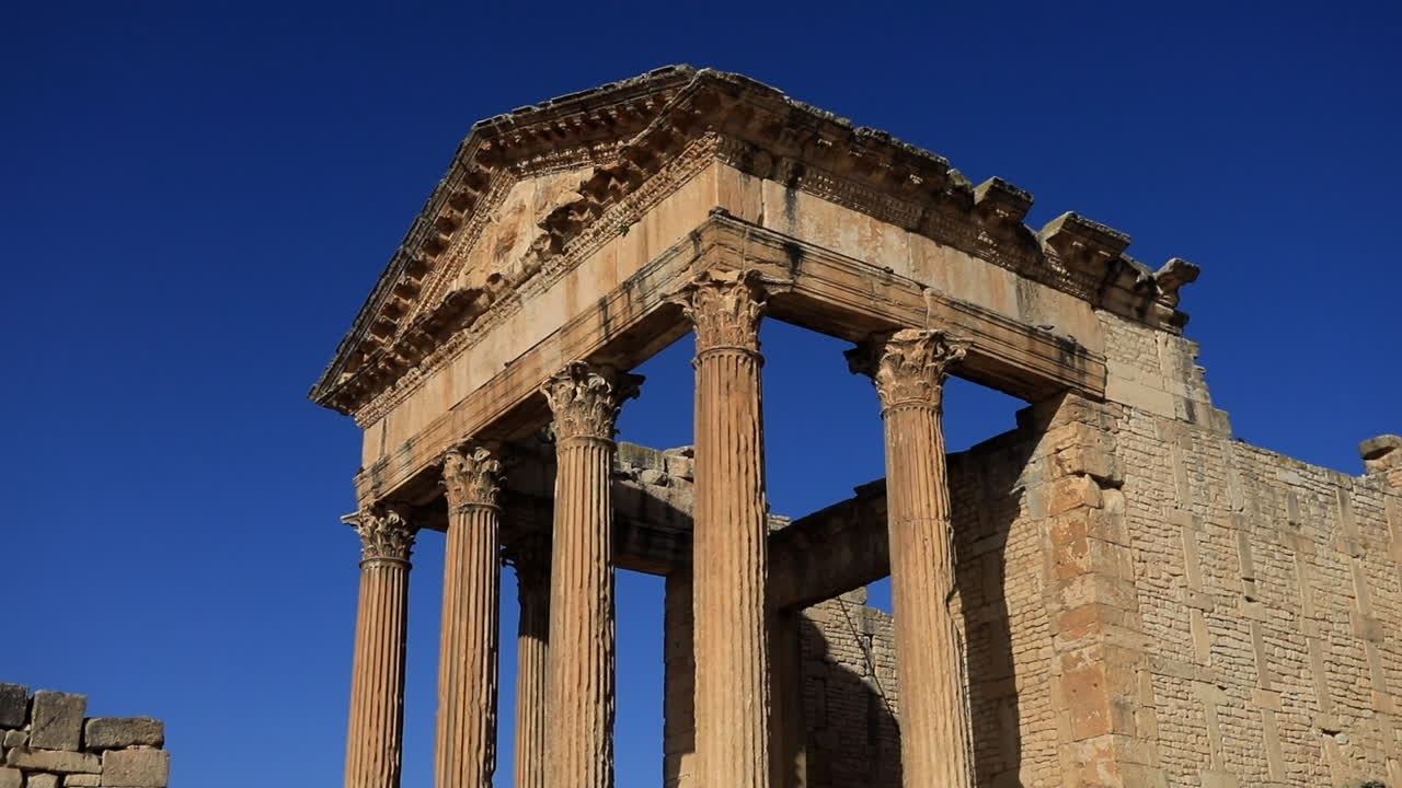 la luz dorada del sol bañando las ruinas romanas de dougga, el fondo del cielo azul claro